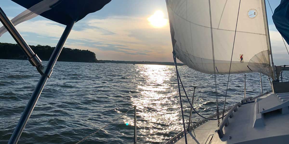 Looking out on a lake from the bow of a sailboat as the sun sets in the distance.